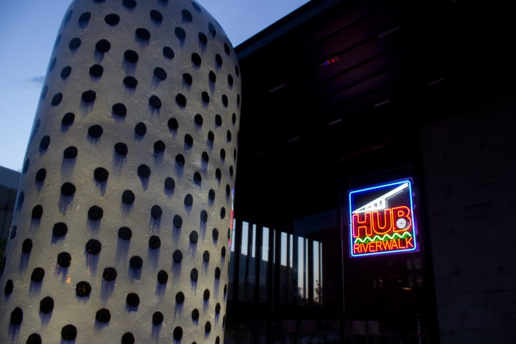 A neon sign and architecture of the Des Moines Riverwalk area near The Hub